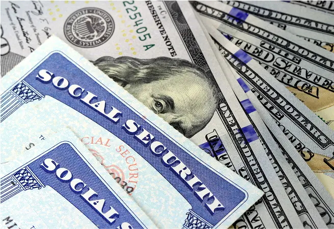 Close-up of Social Security cards on top of various U.S. dollar bills, including a $20 bill featuring Andrew Jackson.